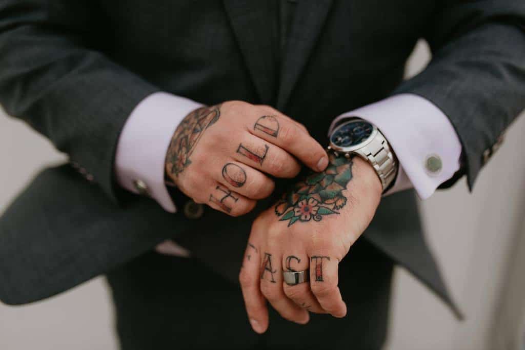 A man in a gray suit showing tattooed hands reading "HOLD FAST"