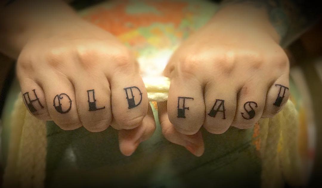 Fingers with "HOLD FAST" tattoos gripping a rope
