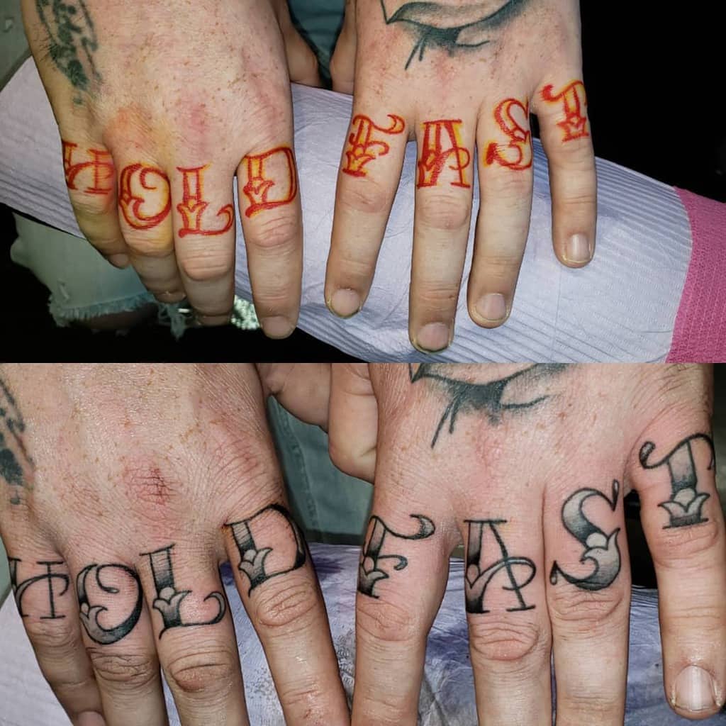 Hands with "HOLD FAST" tattoos on the fingers