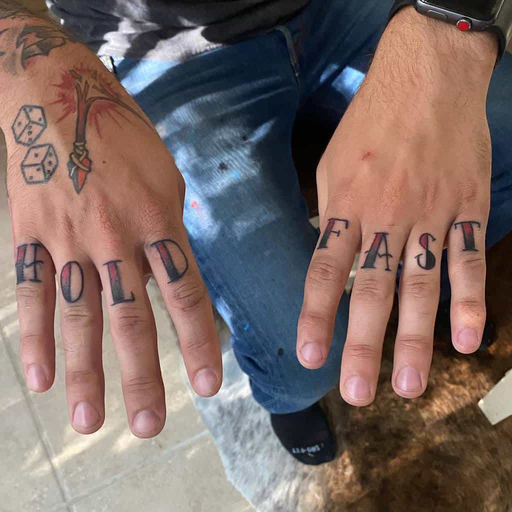 A person's hands with "HOLD FAST" tattooed on the fingers