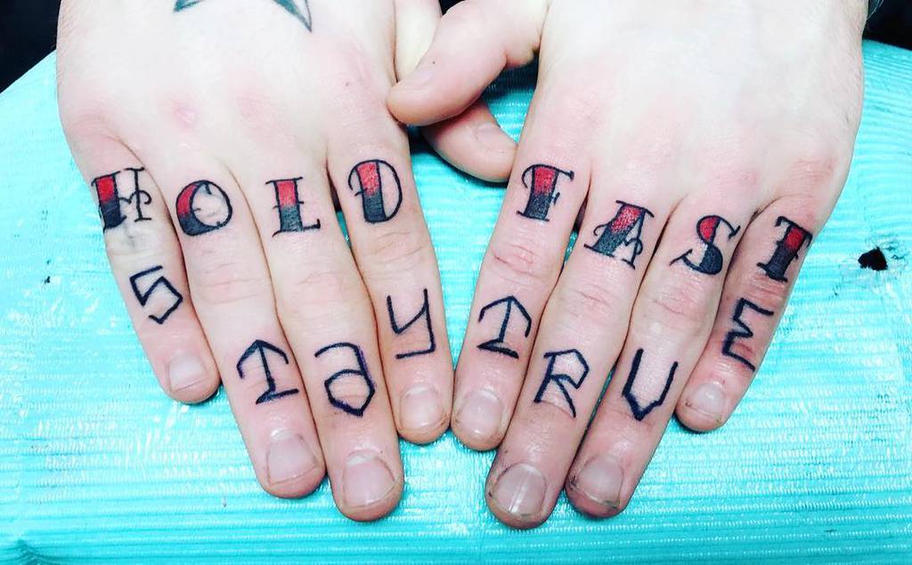 Fingers with "HOLD FAST" and "STAY TRUE" tattoos on knuckles