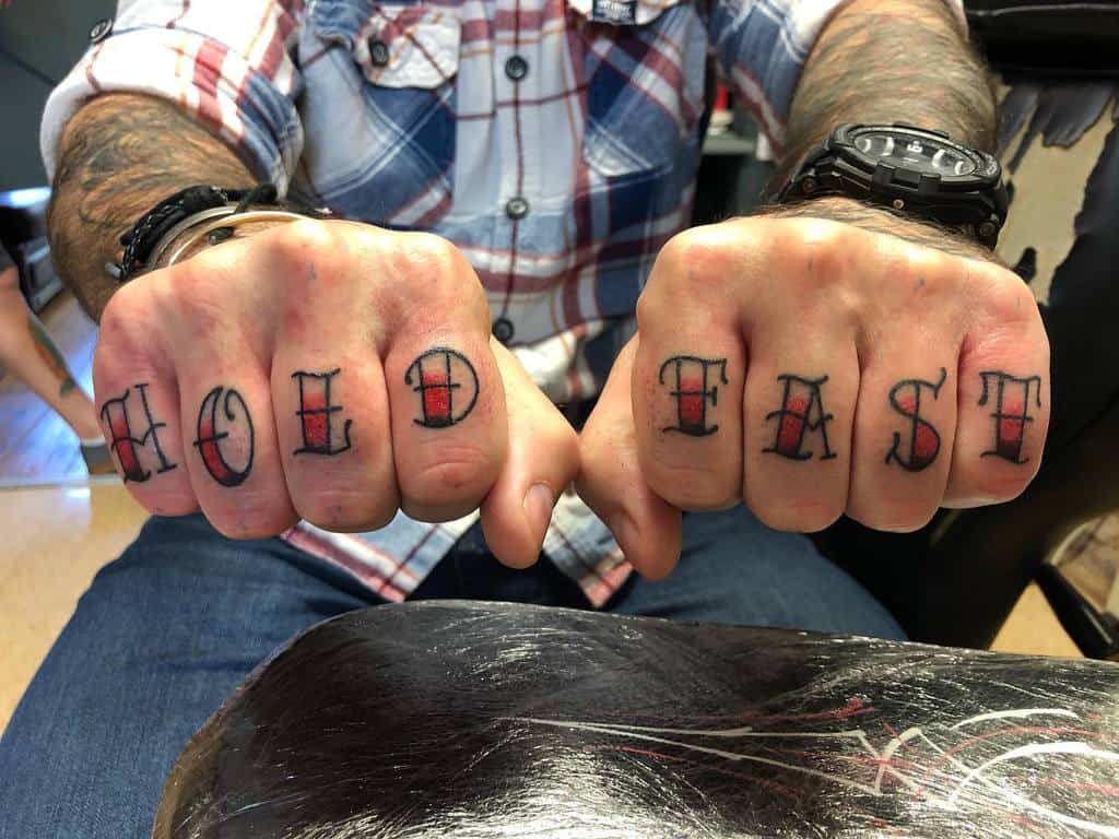 Close-up of tattooed hands with "HOLD FAST" across the knuckles