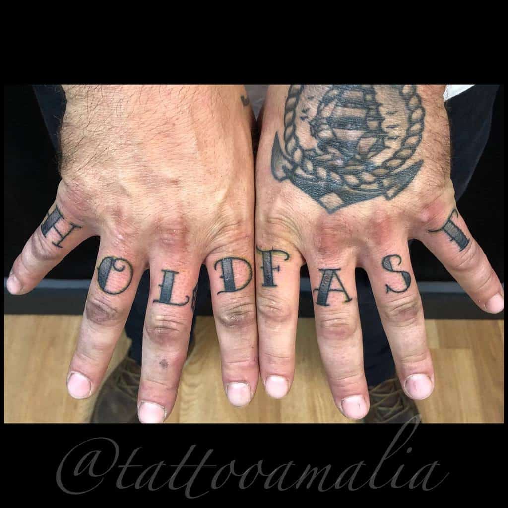 Hands with "HOLD FAST" tattooed across knuckles; ship tattoo on one hand