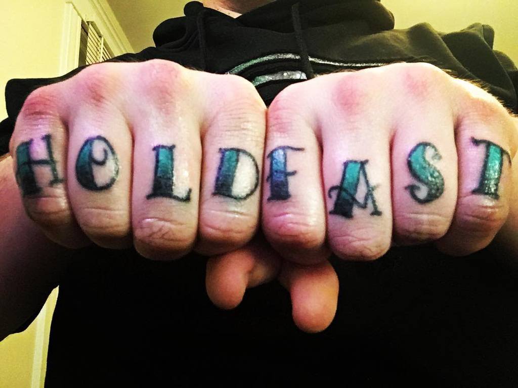 Fingers with "HOLD FAST" tattoos across the knuckles