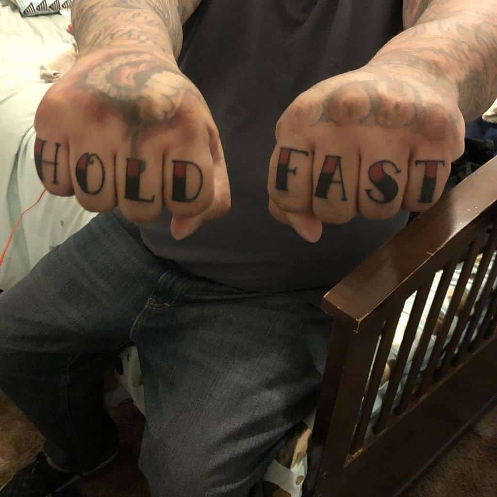 Tattooed knuckles reading "HOLD FAST" on a man’s hands