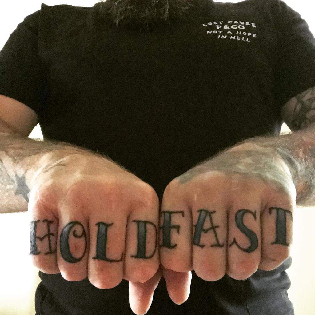 Man showing knuckle tattoos reading "HOLD FAST" 