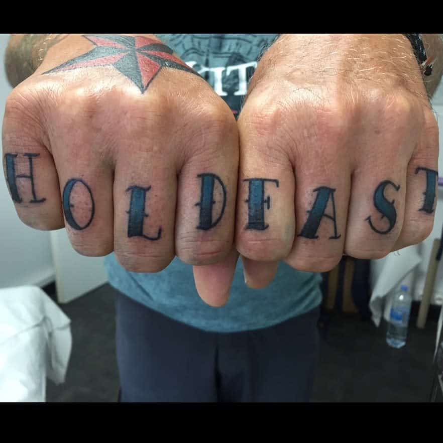 Tattooed fists with "HOLD FAST" and a star tattoo on the wrist