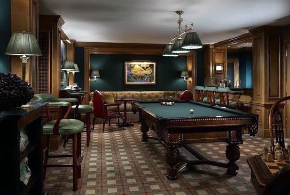 Traditional billiard room with green walls, tufted seating, and a classic wood pool table.