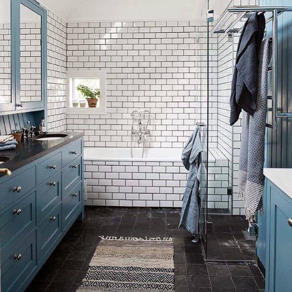 Bathroom with blue vanities, white subway tiles, black flooring, and glass shower.