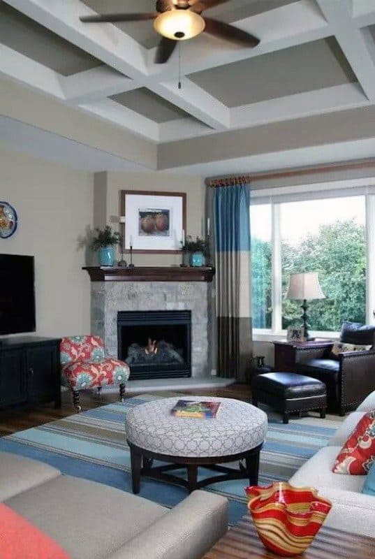 Traditional living room with stone corner fireplace, patterned armchair, ottoman, and coffered ceiling.