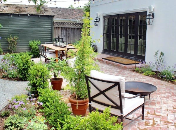 A garden patio with chairs, a table, potted plants, and brick accents around it