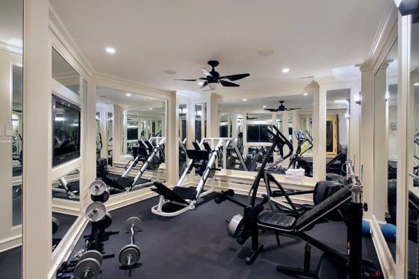 A home gym with diverse exercise equipment, wall mirrors, ceiling fans, and a cozy atmosphere
