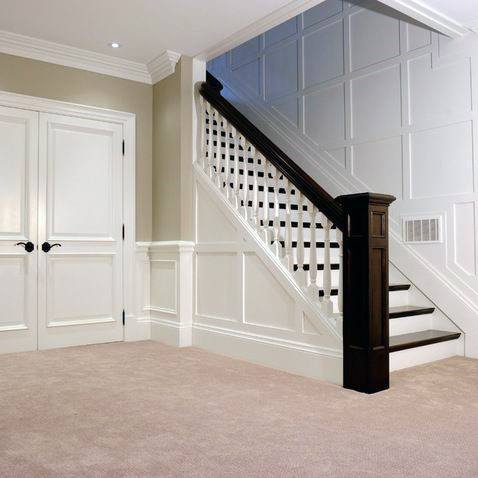 Traditional staircase with white vertical railing and dark wood handrail in a carpeted room.