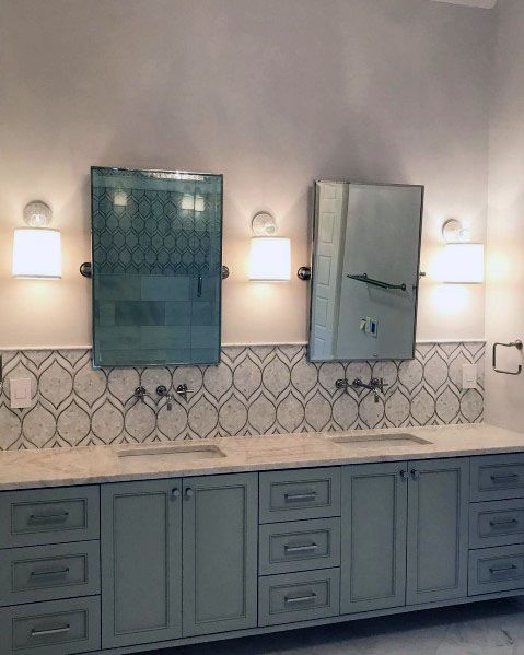 Bathroom with dual vanity, patterned tile backsplash, green cabinets, and two mirrored cabinets.