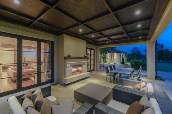 Cozy patio with a fireplace, outdoor seating, and dining area next to a well-lit indoor living space at dusk