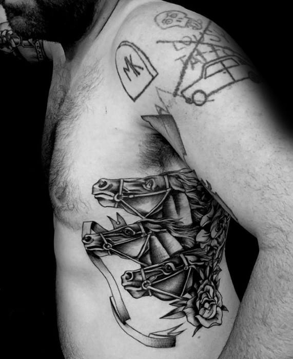 Black and grey side tattoo of three harnessed horse heads with bold shading, metal details, and a rose at the base.