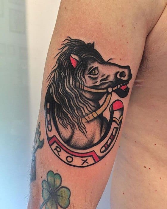 Traditional tattoo of a black horse head with flowing mane inside a red and gold horseshoe labeled “ROX,” placed on the upper arm.