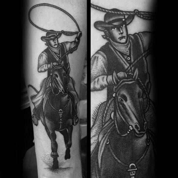 Black and grey tattoo of a cowboy riding a galloping horse with a raised lasso, detailed in bold traditional shading on the forearm.