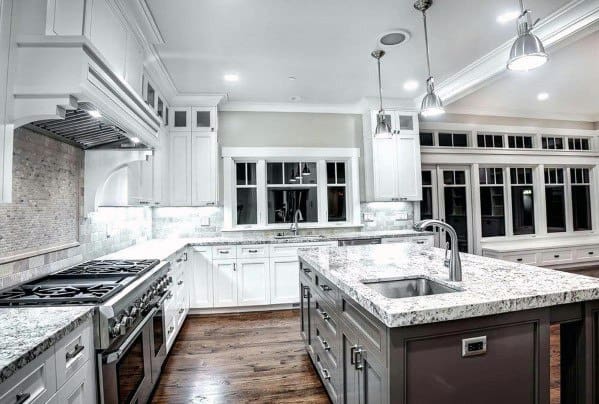 Bright traditional kitchen with white cabinetry, granite countertops, and a soft stone backsplash, complemented by pendant lighting and dark hardwood floors for a refined yet inviting atmosphere