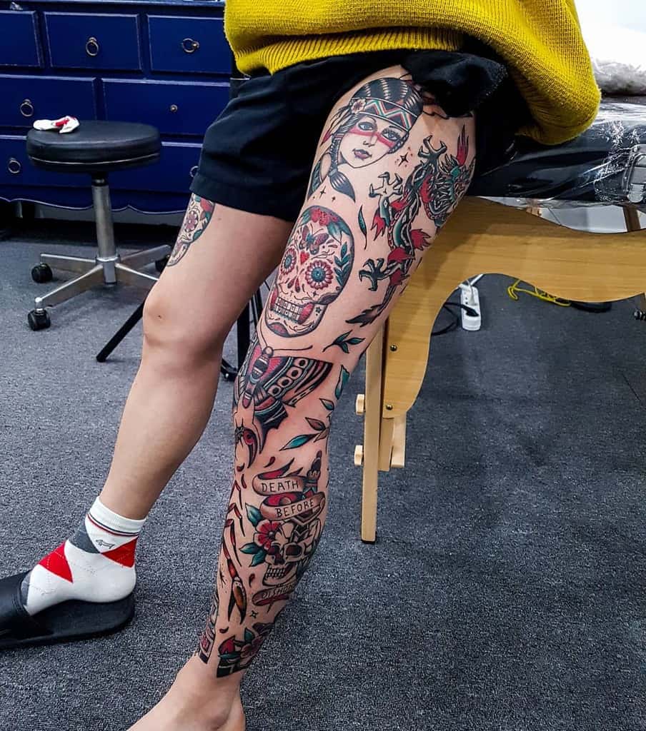 Vivid tattoo leg sleeve, featuring a skull, colorful flowers, a woman with tribal band, dragon, butterfly and a 'Death Before' banner