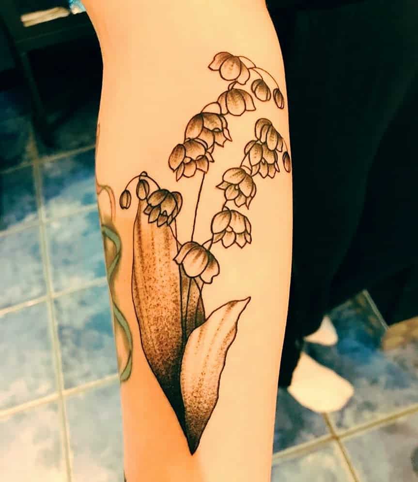 Black and grey Lily of the Valley tattoo, featuring delicate bell-shaped flowers and shaded leaves in a fine line botanical style