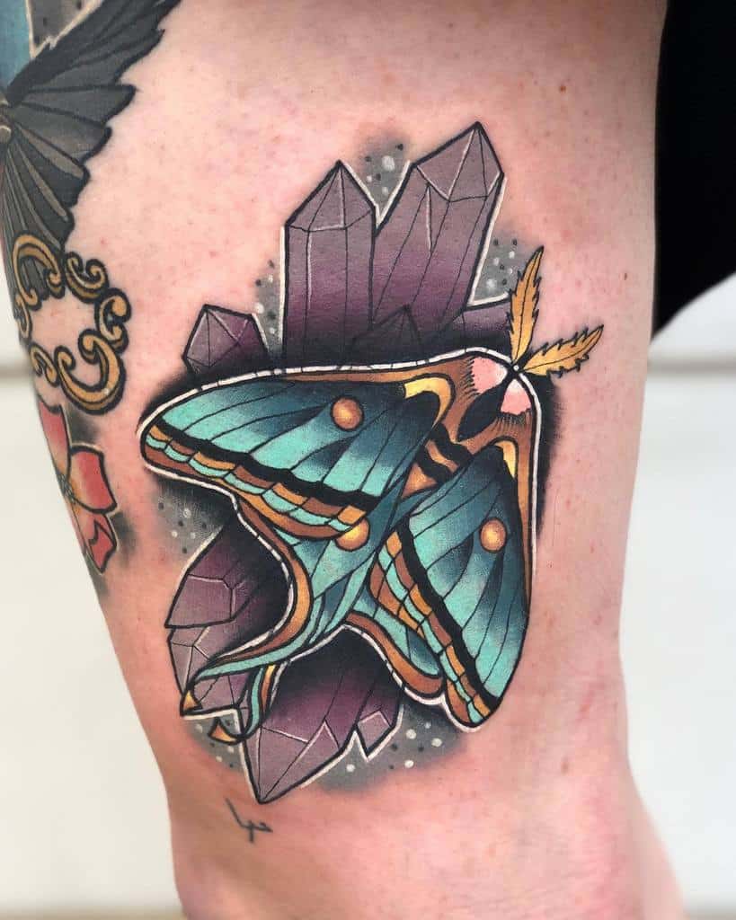 A colorful tattoo of a Luna Moth surrounded by purple crystals and soft shading