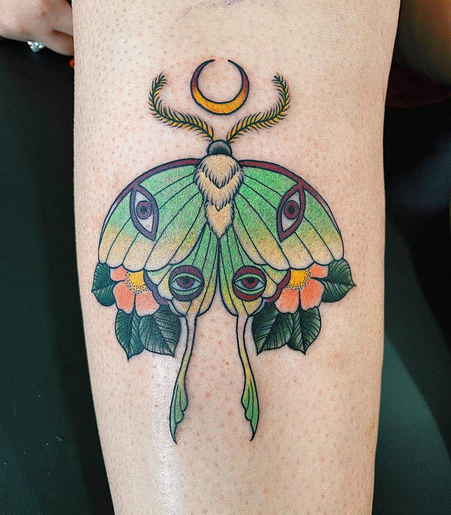 A colorful Luna Moth tattoo, featuring green wings, multiple eyes, floral accents, and a crescent moon above