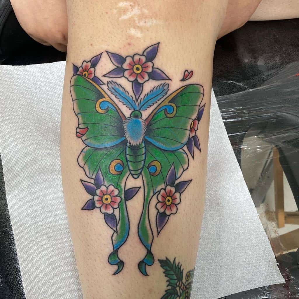 A colorful tattoo of a Luna Moth, with green wings and blue details, surrounded by pink and purple flowers