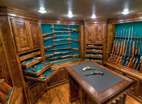 A grand gun room featuring floor-to-ceiling wooden cabinetry, a central display island, and an antler chandelier for a luxurious collector’s ambiance.