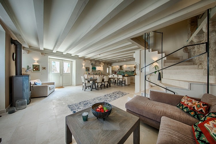 Spacious living room with cozy seating, wooden beams, a modern dining area, and a high ceiling near the kitchen