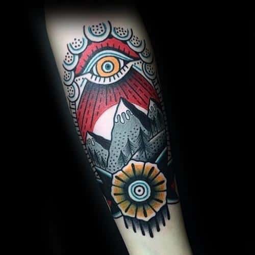 Bold neo-traditional tattoo of snowy mountains with a radiant all-seeing eye above and a geometric sun-like symbol below.