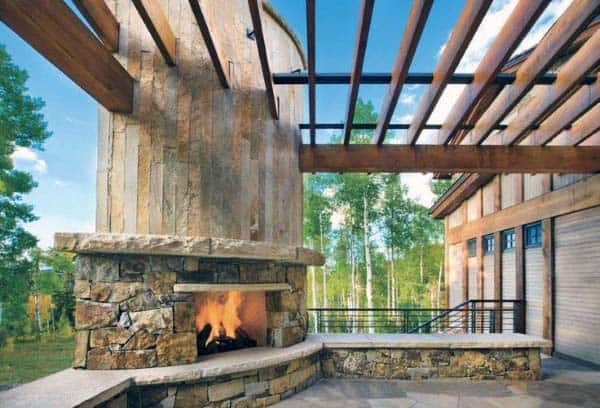 Outdoor stone fireplace on a terrace with wooden pergola and forest view