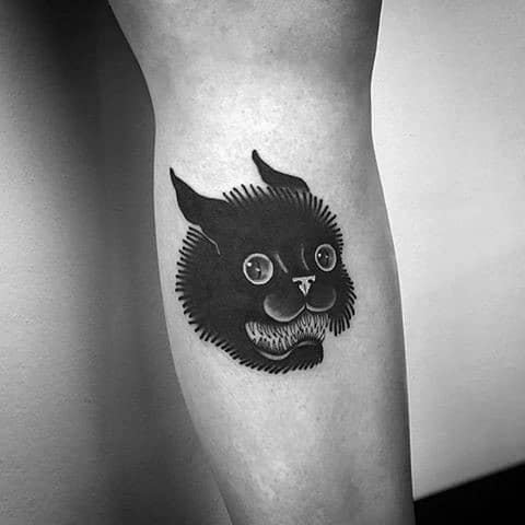 Bold blackwork cat tattoo with exaggerated eyes and sharp teeth, creating a surreal and eerie design on the leg.