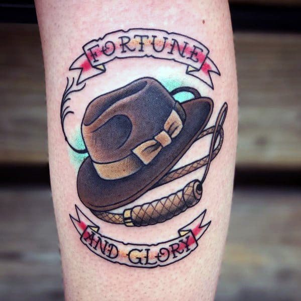 A classic Indiana Jones-inspired tattoo featuring his iconic fedora and whip, framed by a banner reading "Fortune and Glory."