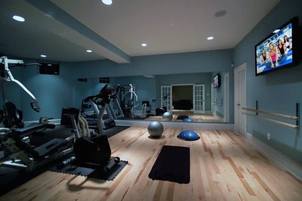 Home gym with wooden floor, large mirror, wall-mounted TV, blue-gray walls—perfect for a cozy workout at home
