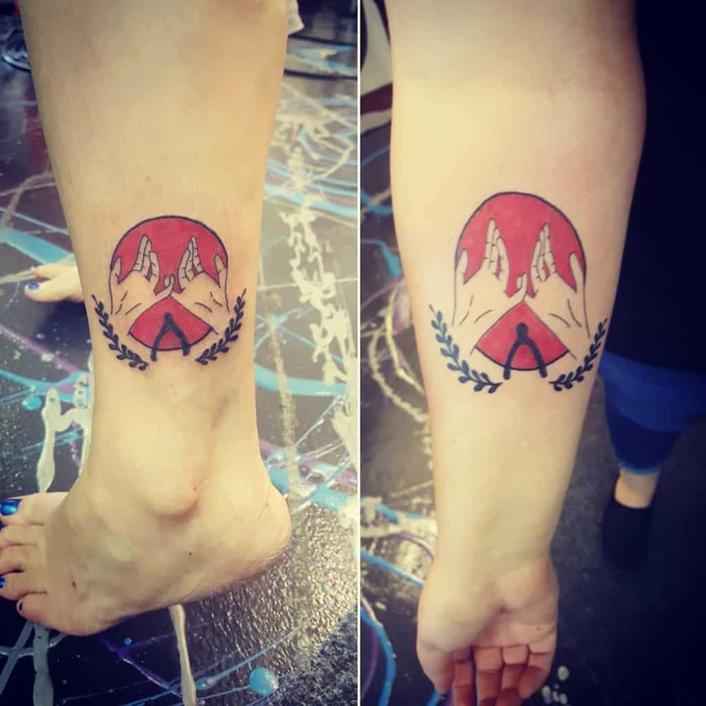 Tattoo of two hands making a pinky promise inside a red circle, with a laurel wreath and an "A" symbol below