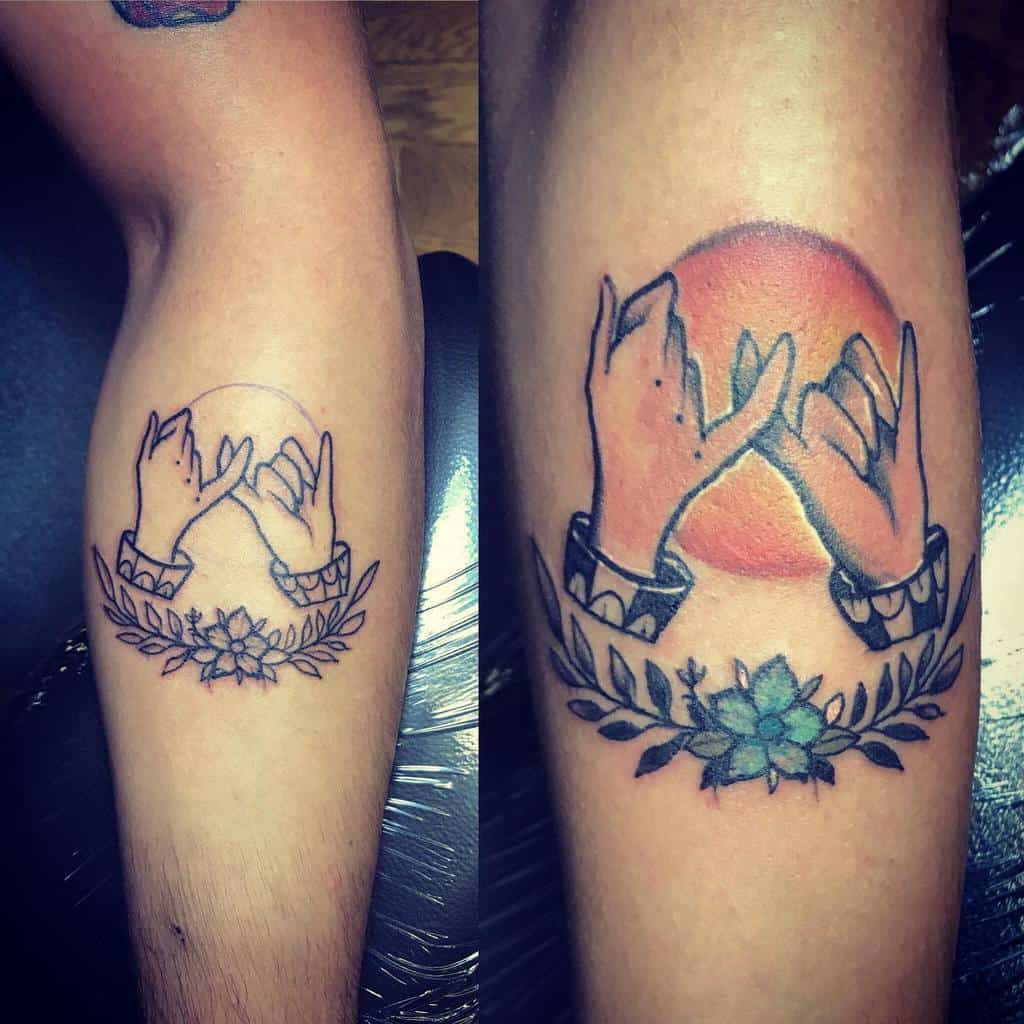Tattoo of two hands making a pinky promise, framed by a floral design, with a red sun in the background