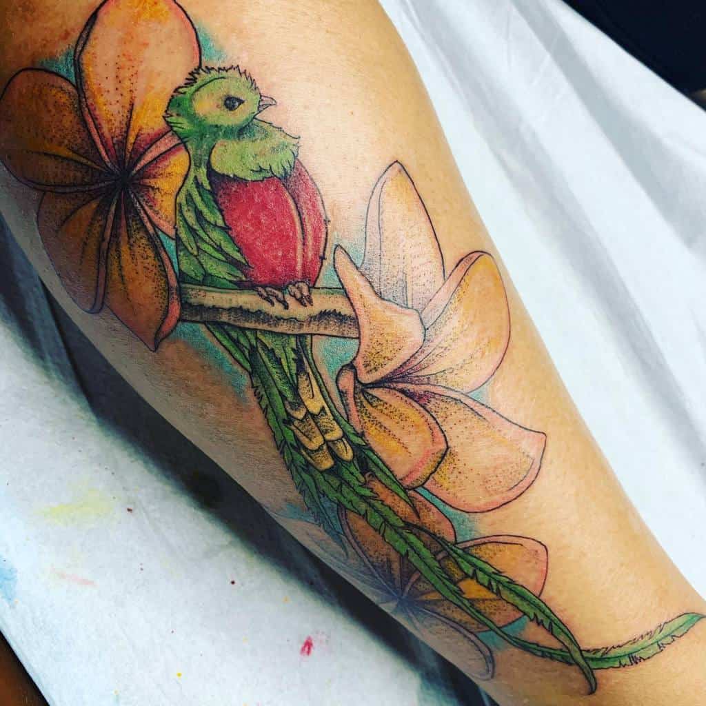 Traditional-style quetzal tattoo on the leg, featuring a vibrant green and red bird perched on a branch, surrounded by large orange flowers with intricate details