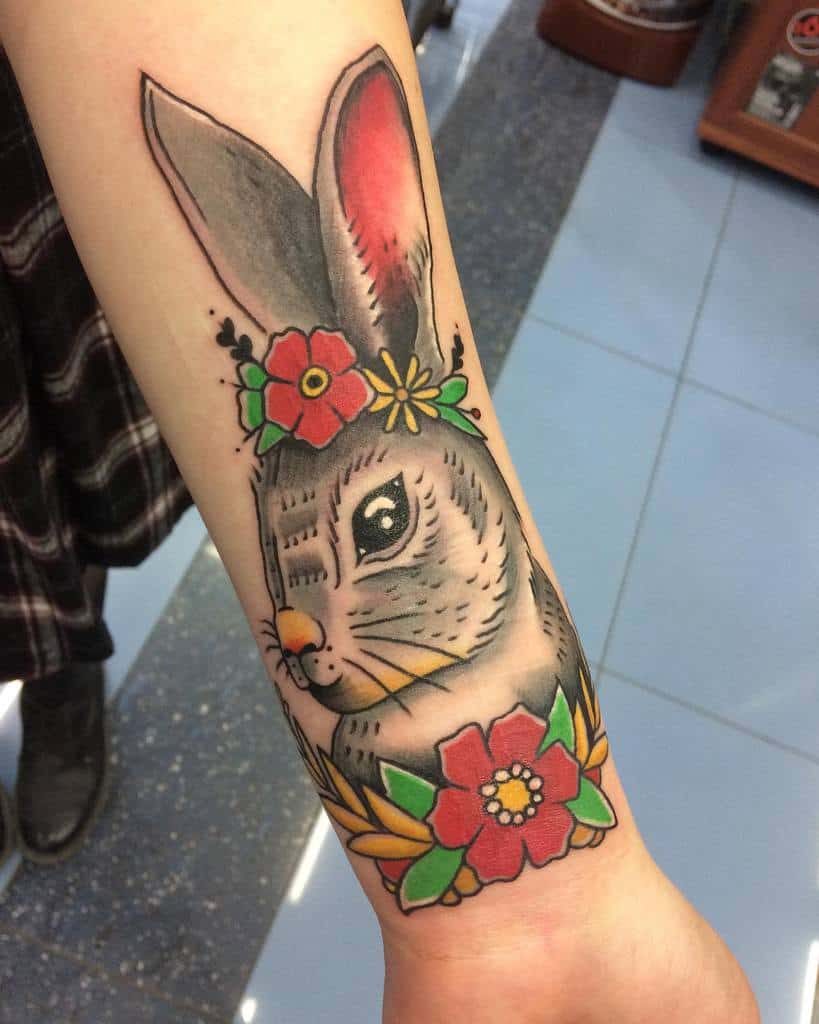 Tattoo of a rabbit with flowers around its neck and head, featuring bright colors and bold outlines