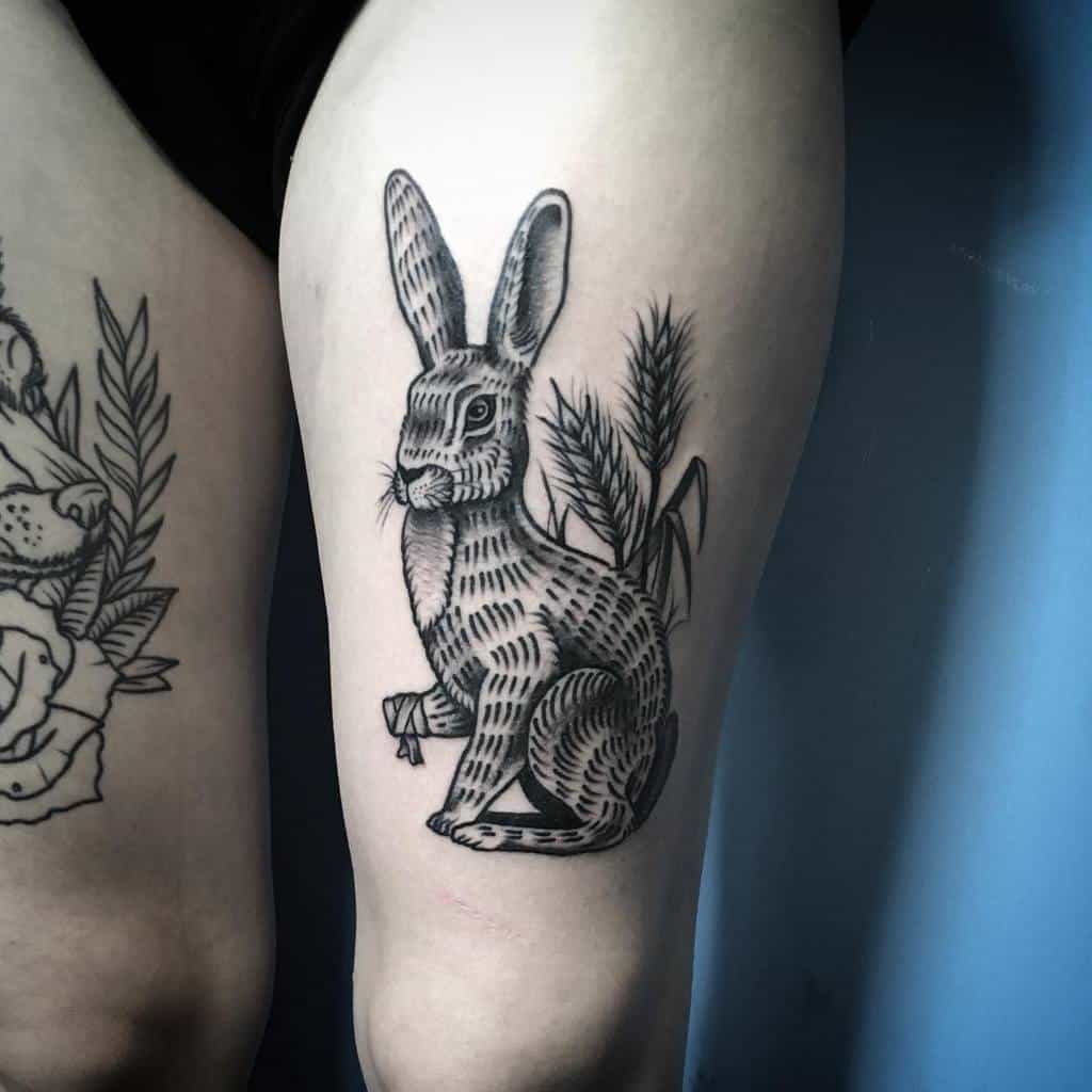 Realistic black and gray tattoo of a sitting rabbit with a bandaged paw, surrounded by detailed plants and foliage