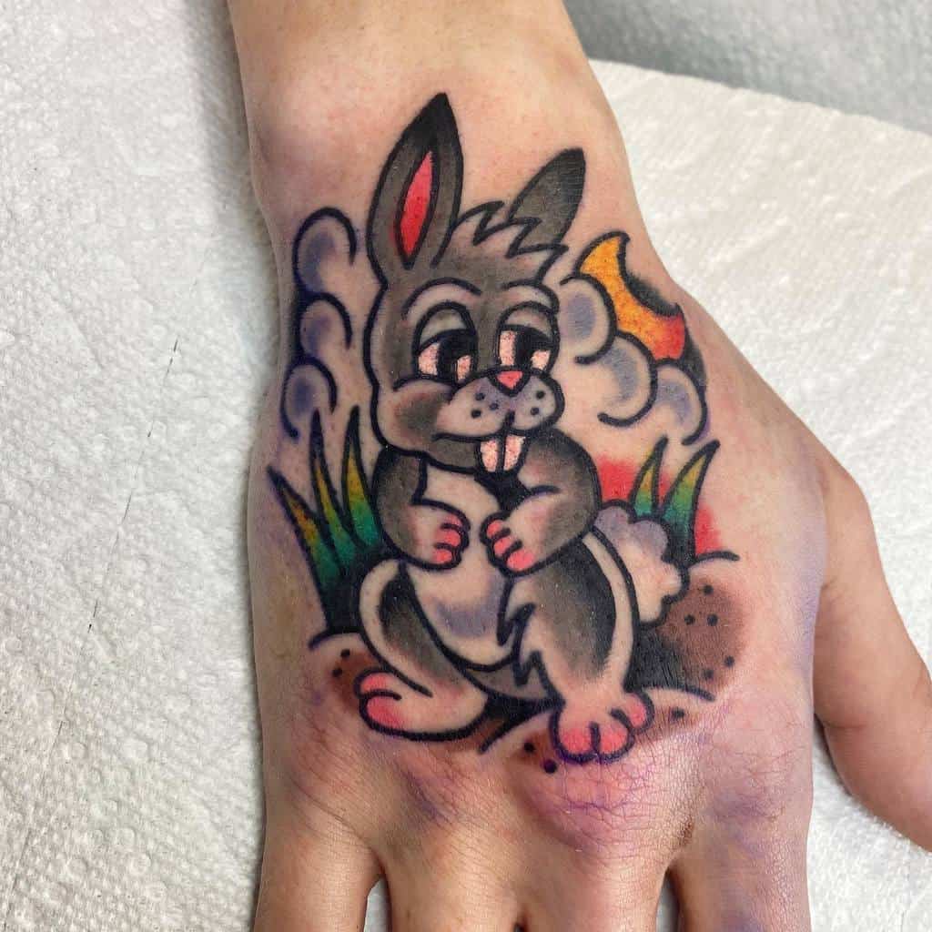 Vibrant tattoo of a cute rabbit with exaggerated features, surrounded by clouds, crescent moon, and grass standing in soil