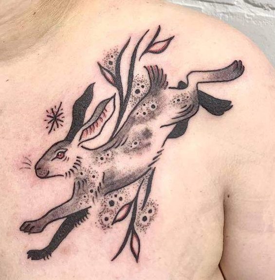 Black and gray tattoo of a leaping rabbit, surrounded by flowing leaves and dotted accents