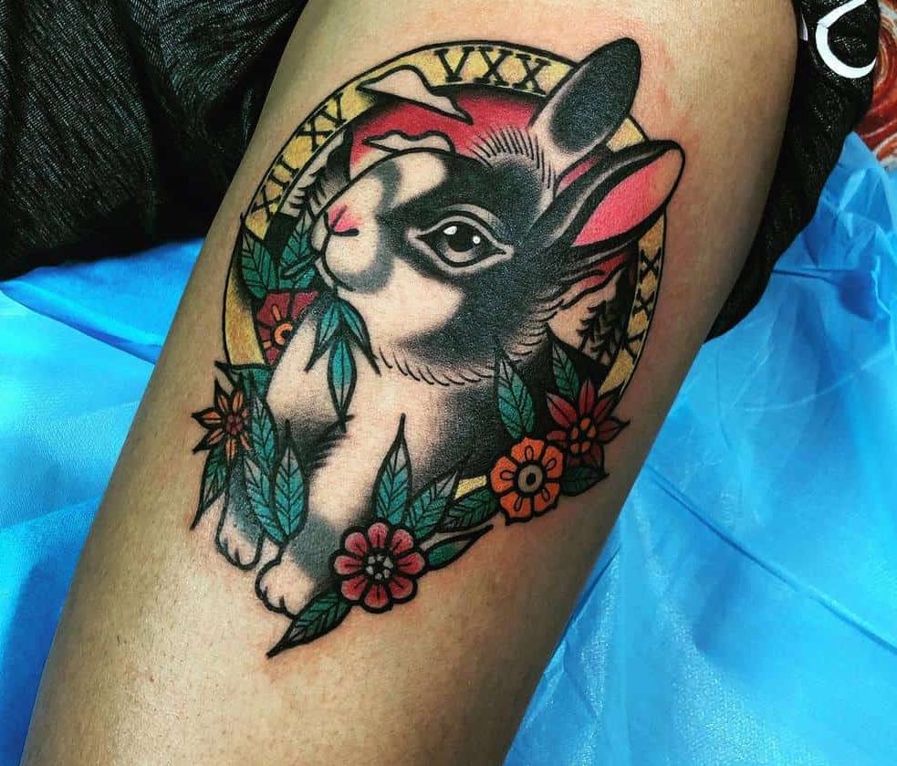 Tattoo of a rabbit with colorful flowers, leaves, trees and Roman numerals in the circle background