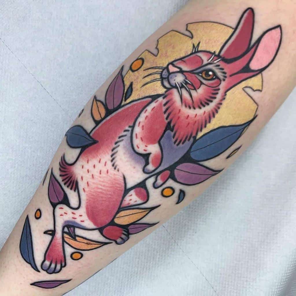 Bold tattoo of a rabbit with vivid pink and orange hues, surrounded by colorful leaves and soft background highlights in yellow and purple