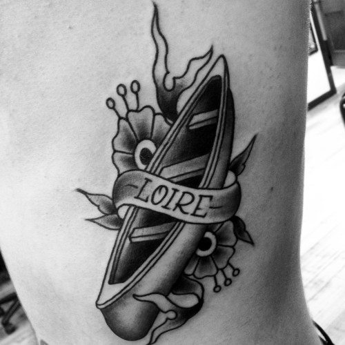 Alt text: Black and grey tattoo of a canoe with a banner reading "LOIRE," surrounded by flowers and decorative elements.