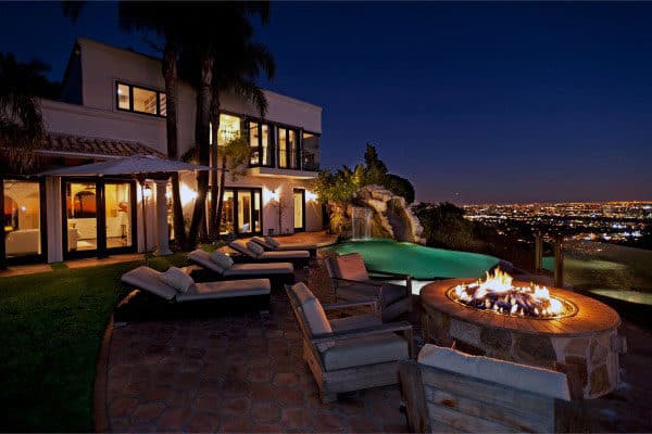 Luxurious house at night with an outdoor fire pit, pool, and city lights view