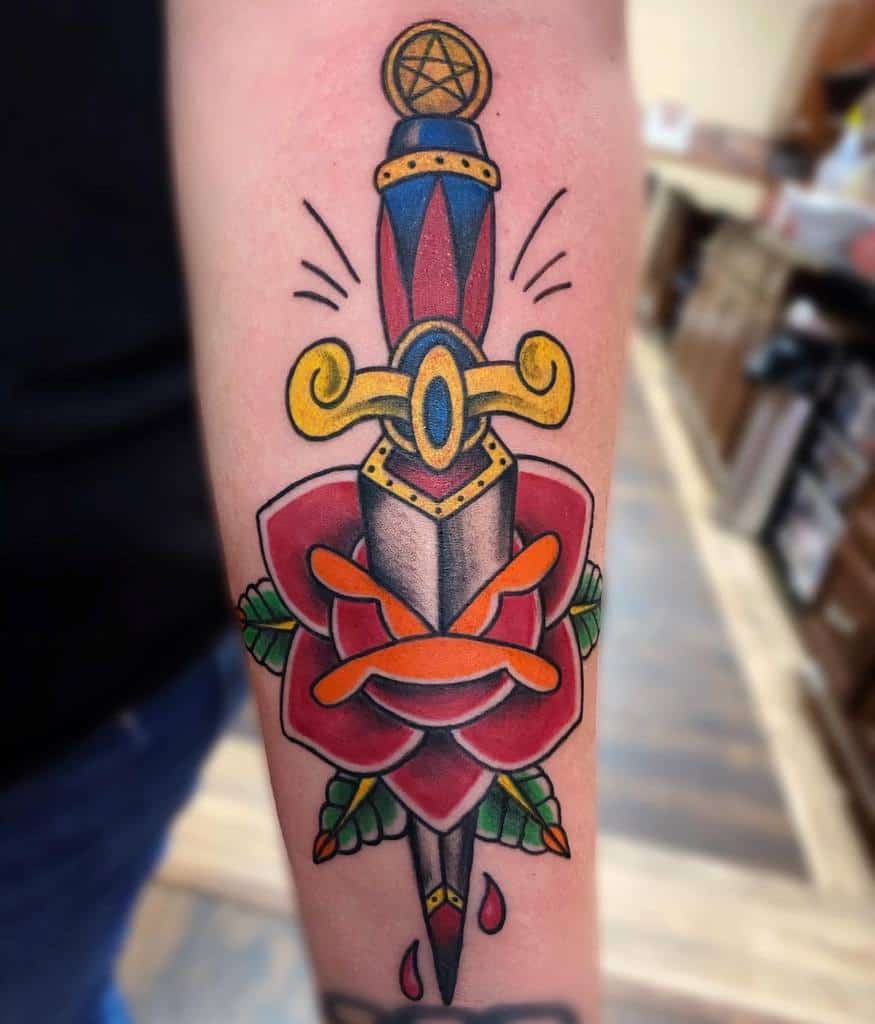 American traditional tattoo of a dagger piercing a red rose with colorful details on an arm