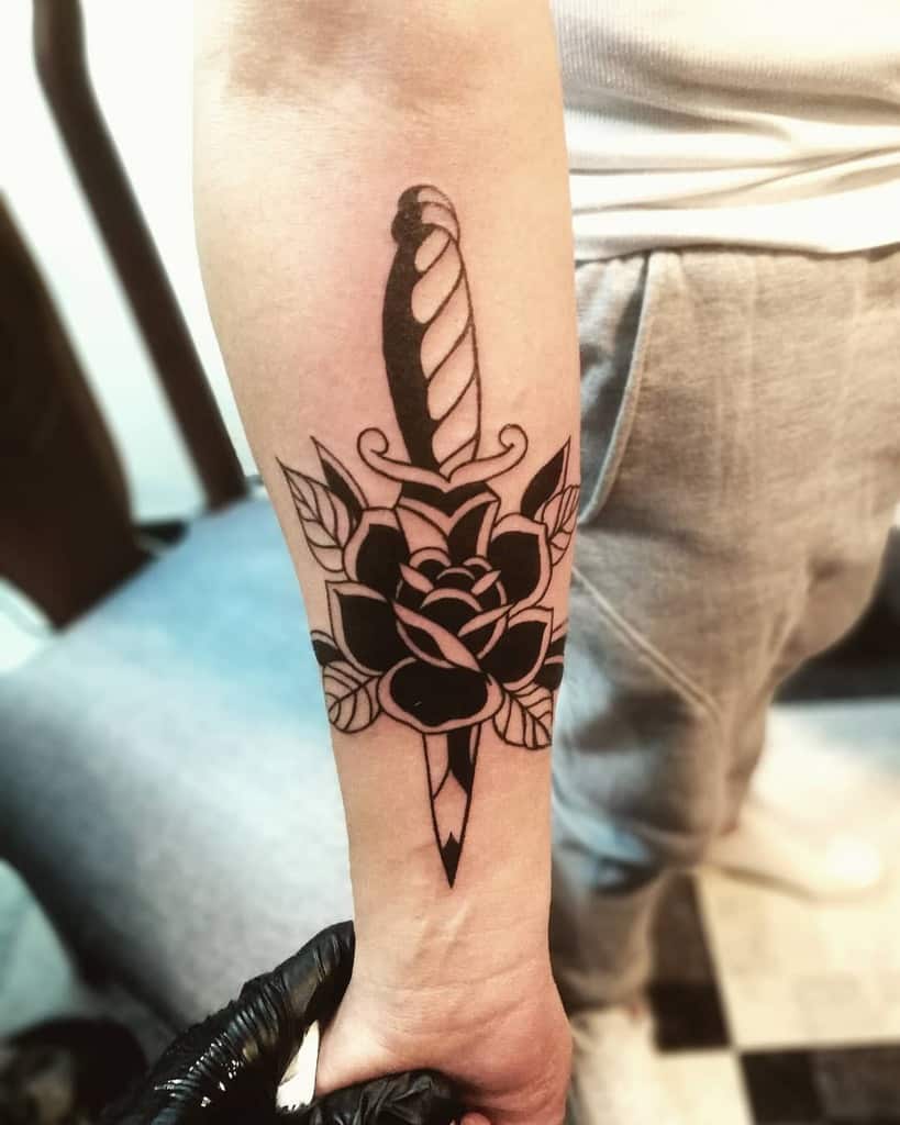 Forearm tattoo of a dagger piercing a rose, shaded in black