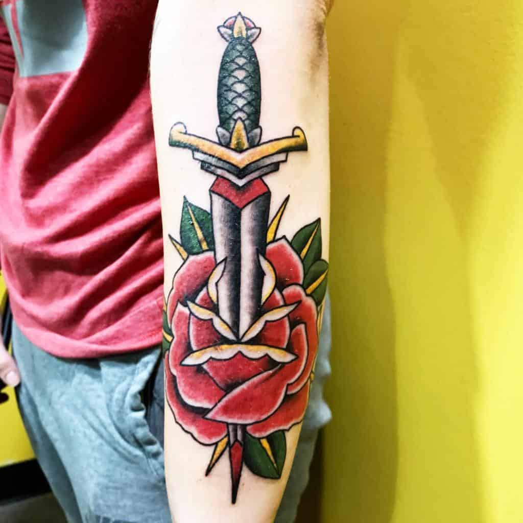 American traditional tattoo of a dagger piercing a rose on a man's forearm