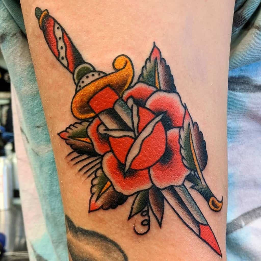 American traditional tattoo of a dagger piercing a red rose on an arm